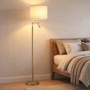 Gold floor lamp glowing beside a bed in a warm bedroom