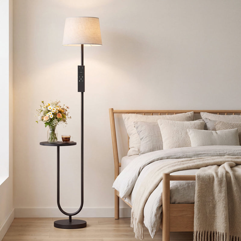 Black floor lamp with shelf beside a bed with cushions and a throw