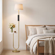Gold floor lamp with shelf beside a bed with cushions and a throw