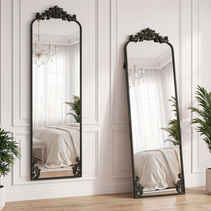 Two black baroque floor mirrors leaning against a bedroom wall reflecting a chandelier