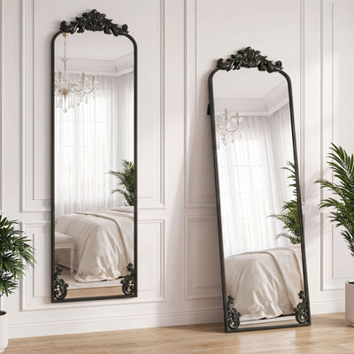 Two black baroque floor mirrors leaning against a bedroom wall reflecting a chandelier