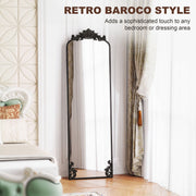 Black baroque floor mirror leaning in a bedroom with a decorative bed and curtains