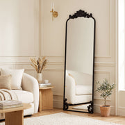 Black baroque floor mirror leaning in a living room beside a cream sofa