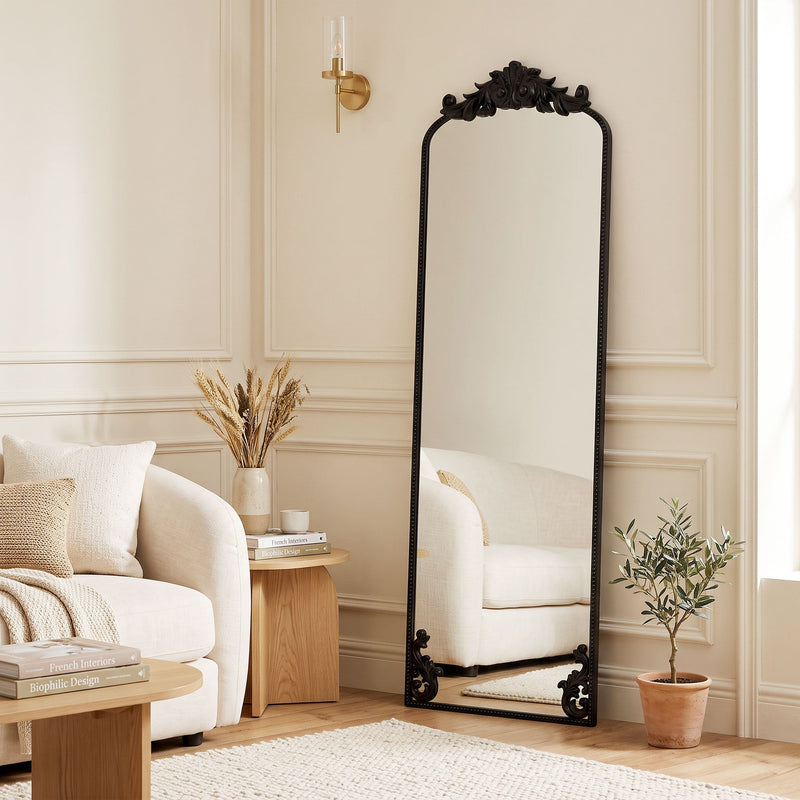 Black baroque floor mirror leaning in a living room beside a cream sofa
