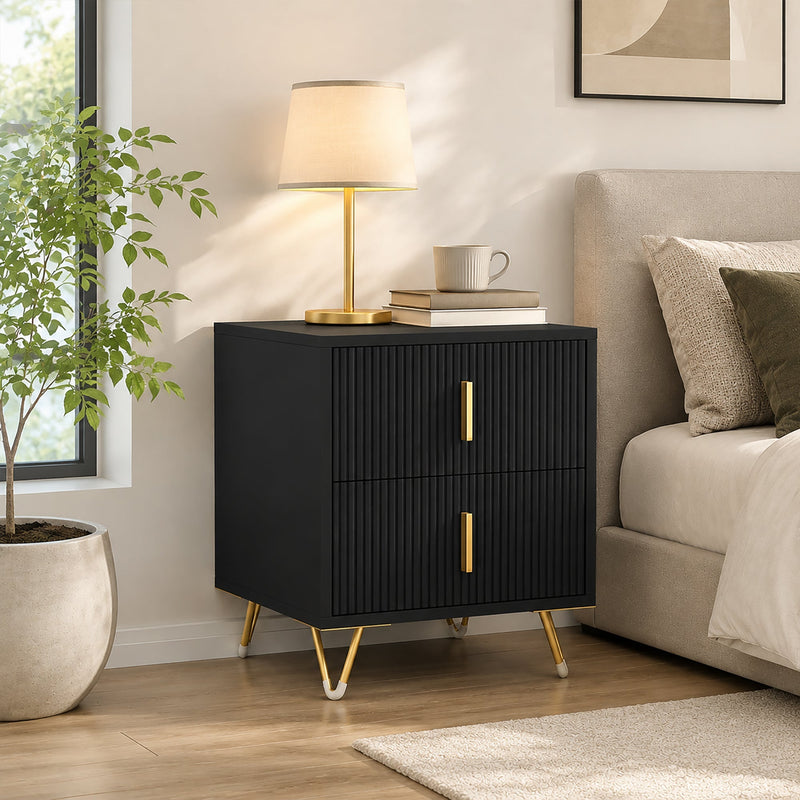 Black and gold-tone fluted bedside table styled beside a bed with lamp and plant