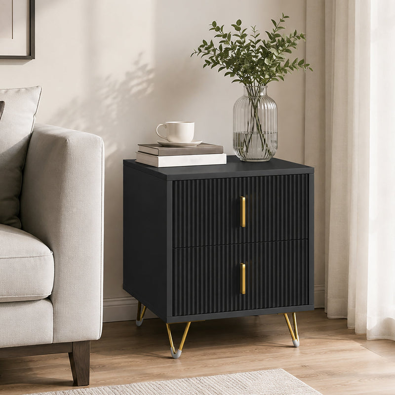 Black bedside table with gold-tone legs styled in a living room with a plant