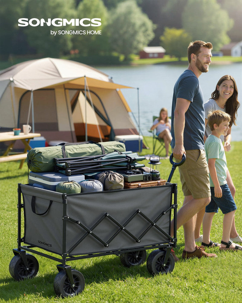Family pulling the loaded dove grey camping cart across grass at a lakeside campsite