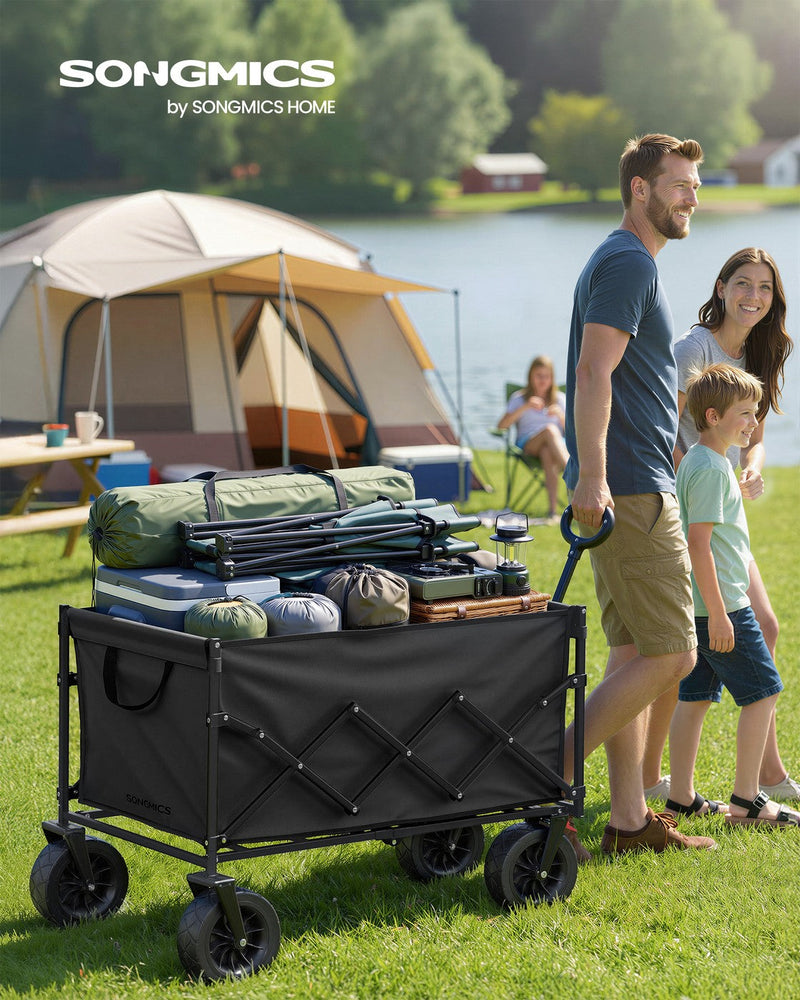Family pulling the loaded ink black camping cart across grass at a lakeside campsite