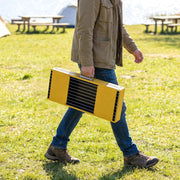 Yellow Outsunny BBQ grill folded and carried by hand across grass at a campsite