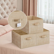 3 sand beige fabric storage bins on a bed with a close-up of the label tag