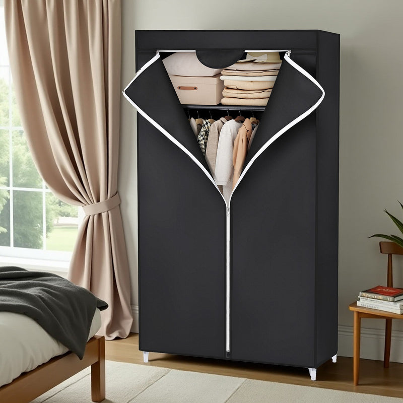 Black fabric wardrobe styled beside a bed, unzipped showing hanging clothes and storage boxes