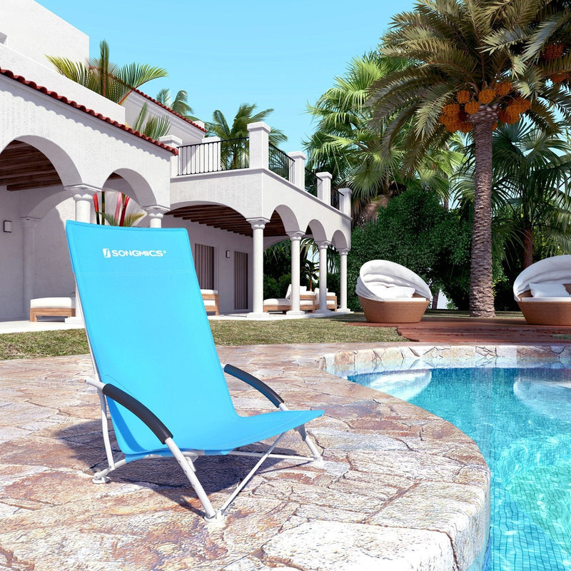 The blue beach chair set up on a poolside terrace with palm trees and a villa behind