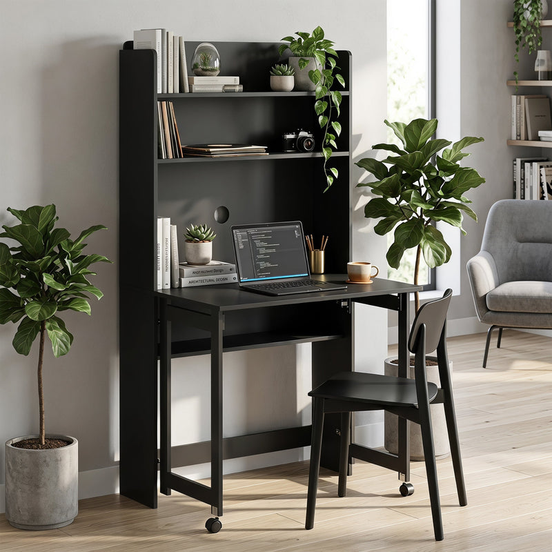 Black folding desk open in a bright room with a laptop on the tabletop, tall plants either side and a black dining chair pulled up to it