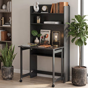 Black folding desk open against a wall with books and a clock on the shelves, a glass lamp on the desktop and a plant beside it
