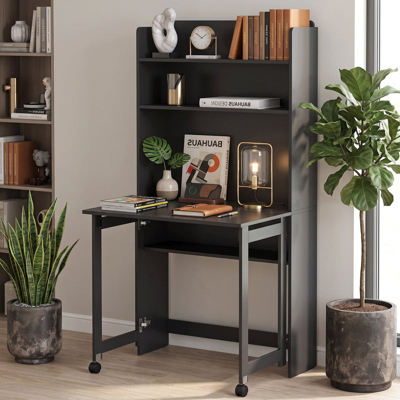 Black folding desk open against a wall with books and a clock on the shelves, a glass lamp on the desktop and a plant beside it