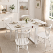 White dining table set for four with sage green chairs in a bright dining room