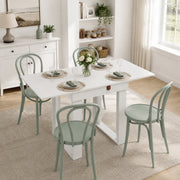 White dining table extended to seat four with sage green chairs in a dining nook
