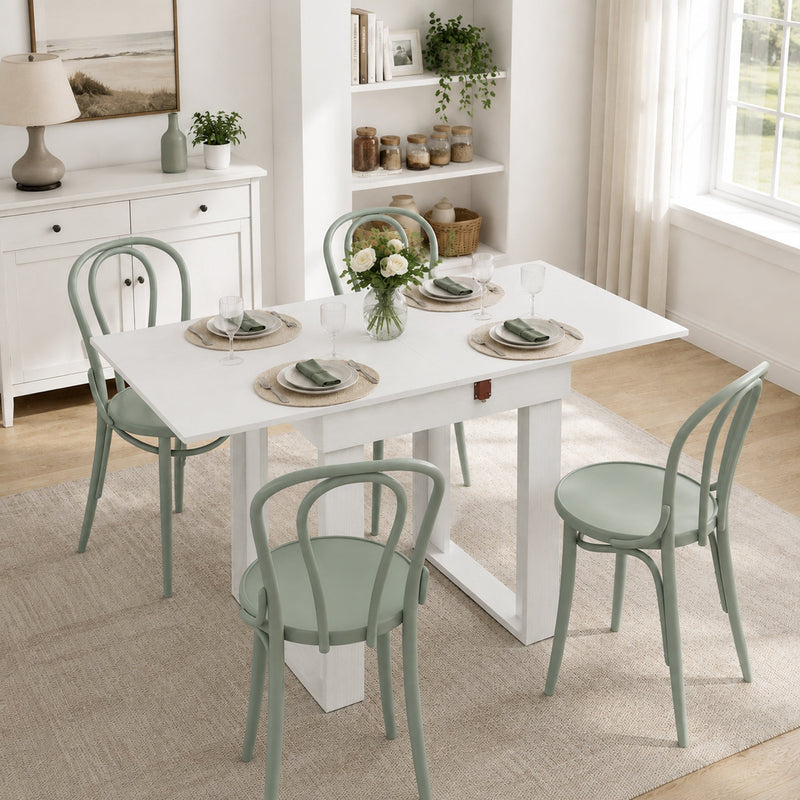 White dining table extended to seat four with sage green chairs in a dining nook