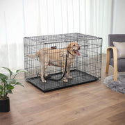 Black metal dog crate with a Labrador inside, set in a living room beside an armchair