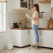 Woman standing on the folding step stool to reach a kitchen wall cupboard