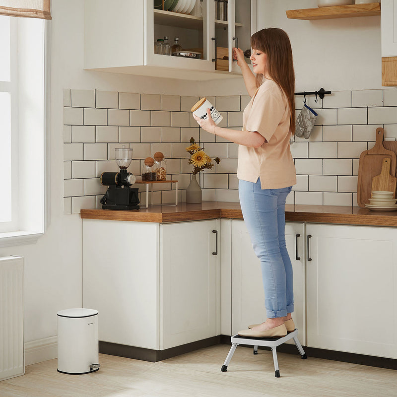 Woman standing on the folding step stool to reach a kitchen wall cupboard