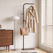 Black clothes rail holding a trench coat and leather tote bag beside a wooden chest of drawers