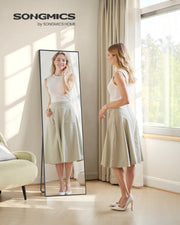 Full length mirror standing against a bedroom wall beside a woman checking her outfit