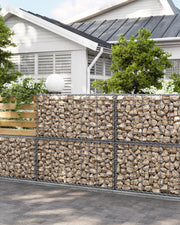 Stone-filled gabion baskets used as a garden boundary wall in front of a house