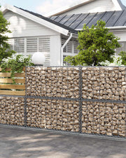 Stone-filled gabion basket forming a garden boundary wall in front of a house