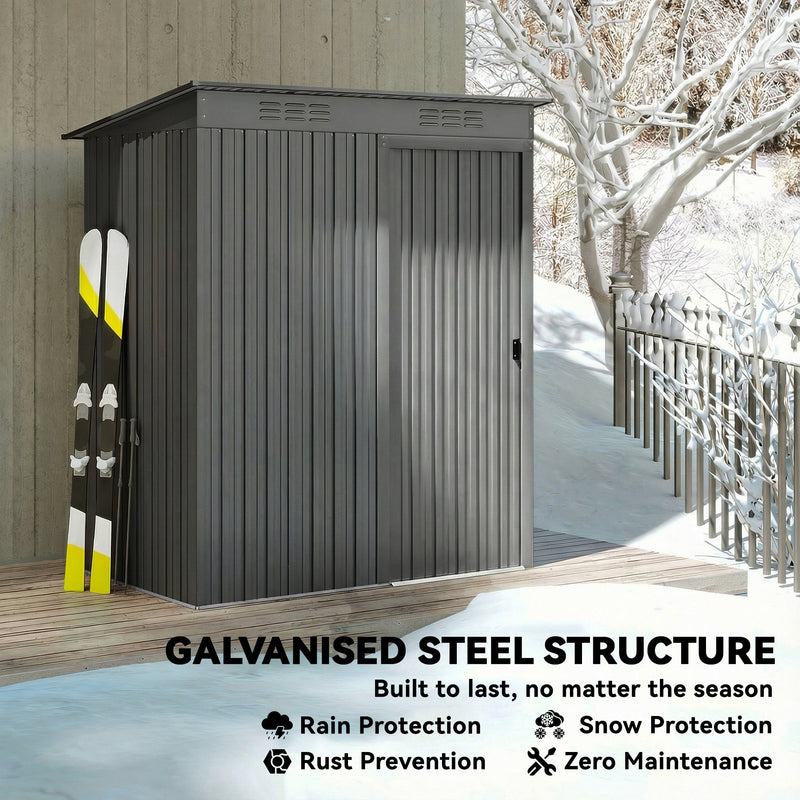 Light grey metal garden shed standing in snow with skis leaning against the side