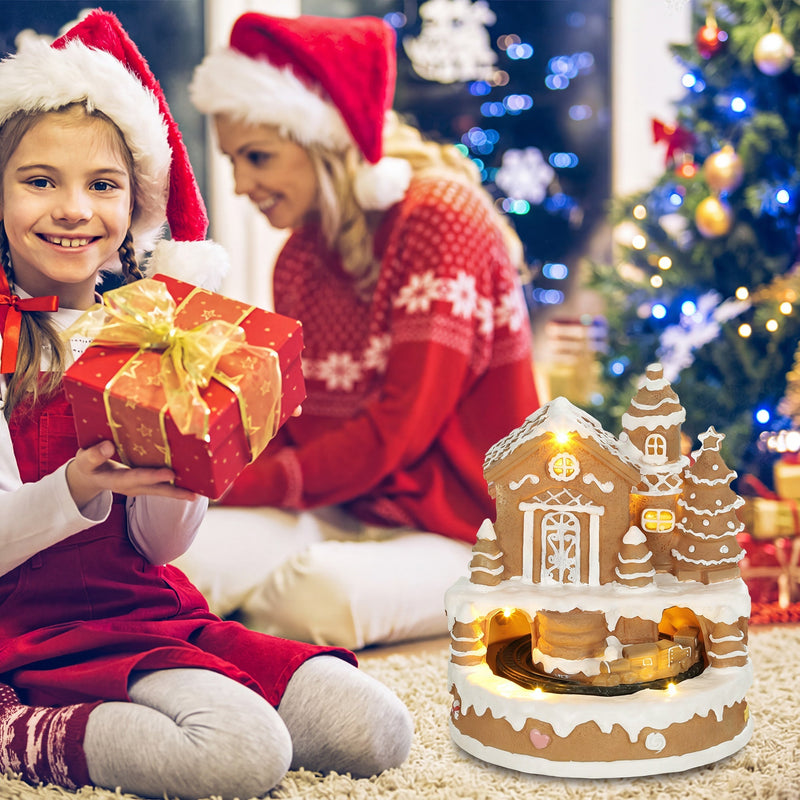 Child and adult in Santa hats with a gift beside the lit house