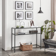 Black console table in a hallway beneath a gallery wall of framed prints