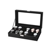 Black glass-lid watch box open showing 12 velvet-lined compartments holding watches