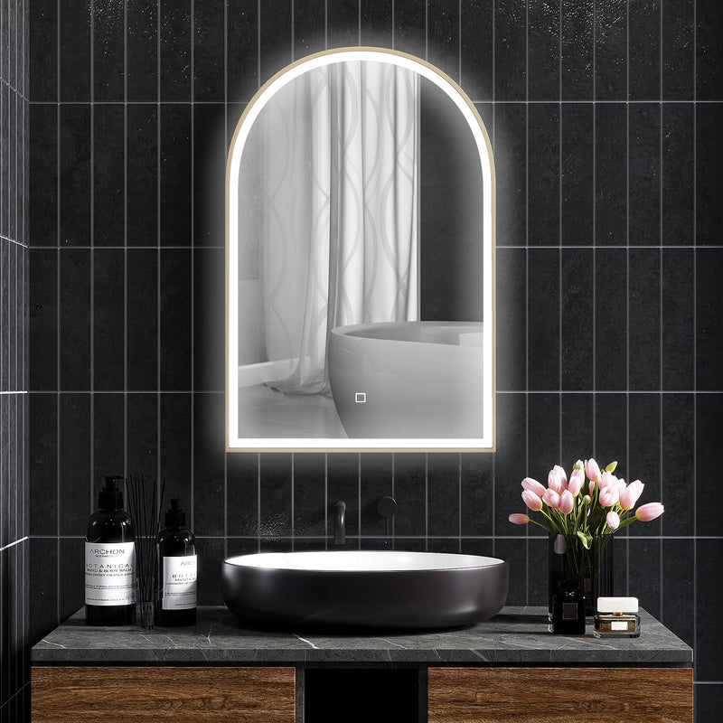 Lit arched mirror on a dark tiled wall above a black basin and tulips