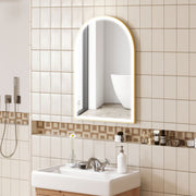 Lit arched mirror on a cream tiled bathroom wall above a white basin