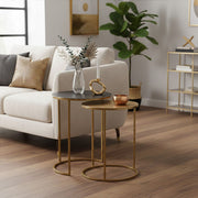 The two gold nesting tables separated either side of an armchair in a room setting