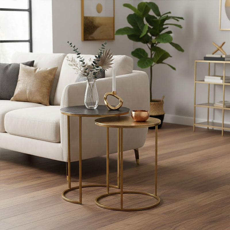 The two gold nesting tables separated either side of an armchair in a room setting