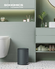 Small pedal bin standing beside a toilet in a pale green bathroom