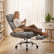 Woman reclining in the grey office chair with the footrest out and a cat beside her