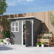 Dark grey 7x4ft metal garden shed on a paved garden patio with the door open, showing tools and boxes on the shelves inside