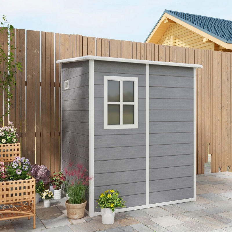 Grey plastic shed closed on a paved patio beside a fence with flower baskets and pots