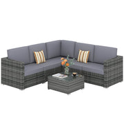 Grey rattan corner sofa set with grey cushions and glass coffee table on a white background