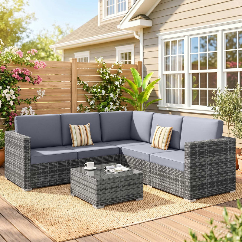 Grey rattan corner sofa set with coffee table styled on a garden patio beside a house