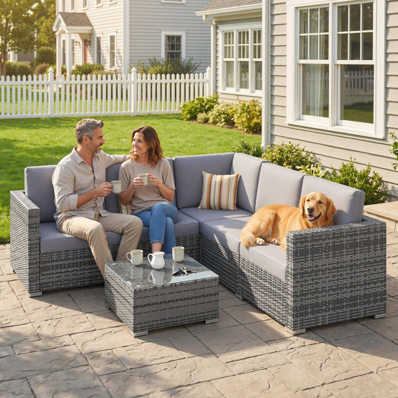 Couple with a dog on the grey rattan corner sofa with coffee table on a paved patio
