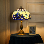 Lit stained glass table lamp on a cloth-covered side table beside a picture frame