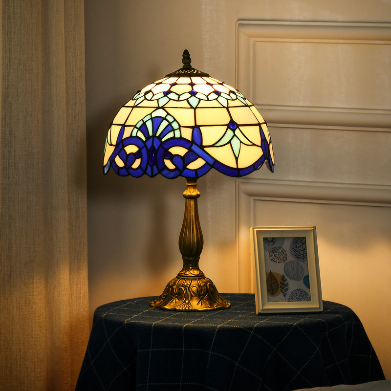 Lit stained glass table lamp on a cloth-covered side table beside a picture frame
