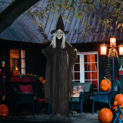 Hanging witch decoration suspended from a porch roof above lit pumpkins at night