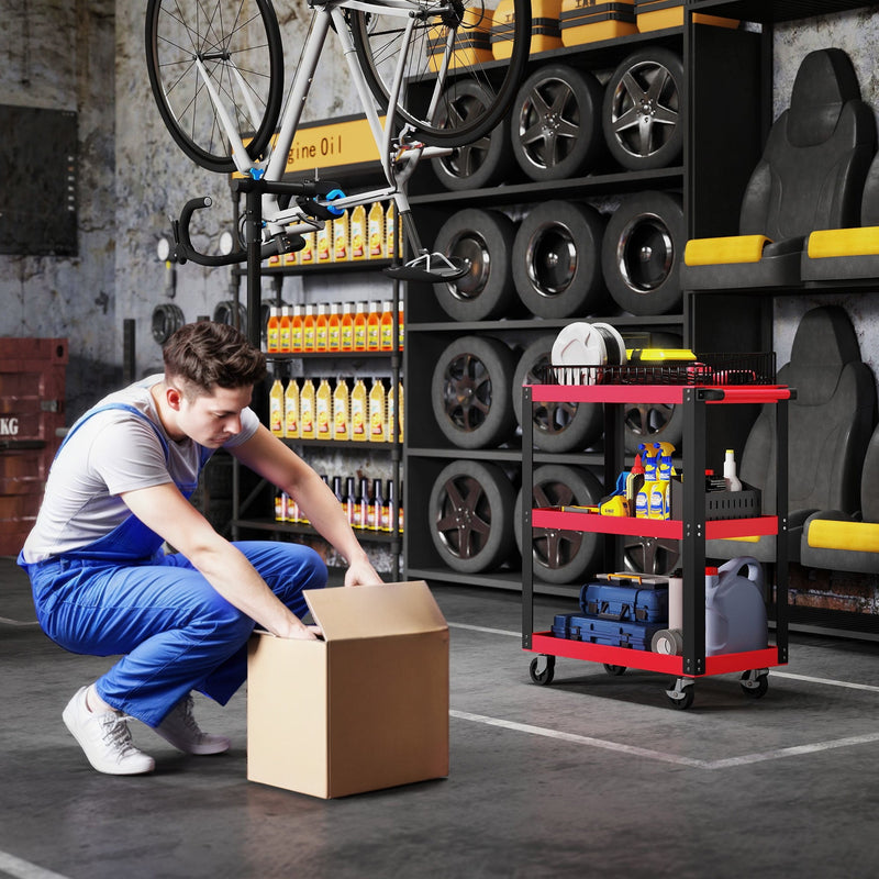 Mechanic crouching by a cardboard box with the loaded tool trolley in the garage behind