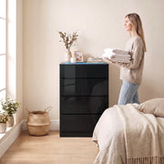 Woman holding folded towels next to the black high gloss chest of drawers in a bedroom