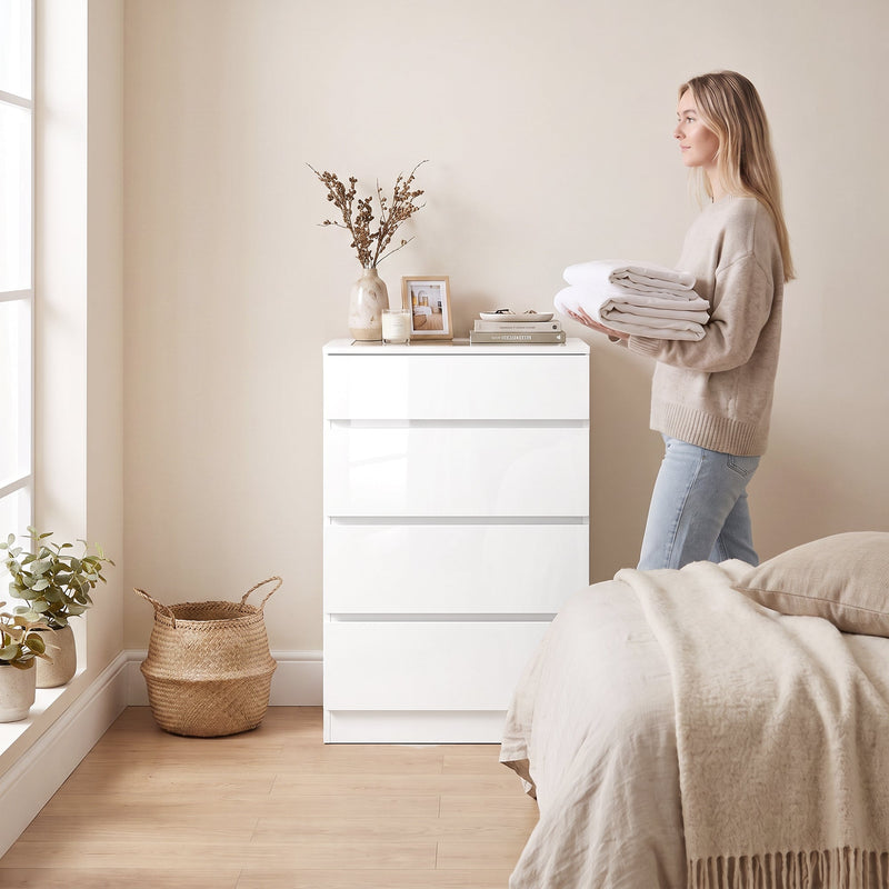 Woman placing folded towels on top of the white gloss chest of drawers in a bedroom